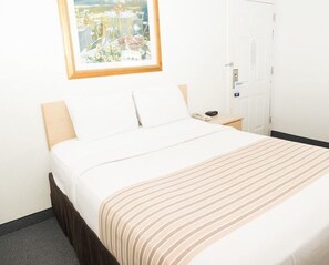 A hotel room with a bed, a bedside table with a phone, a window with a view, and a door. - Suburban Studios Lakeland North I-4 (Lakeland)