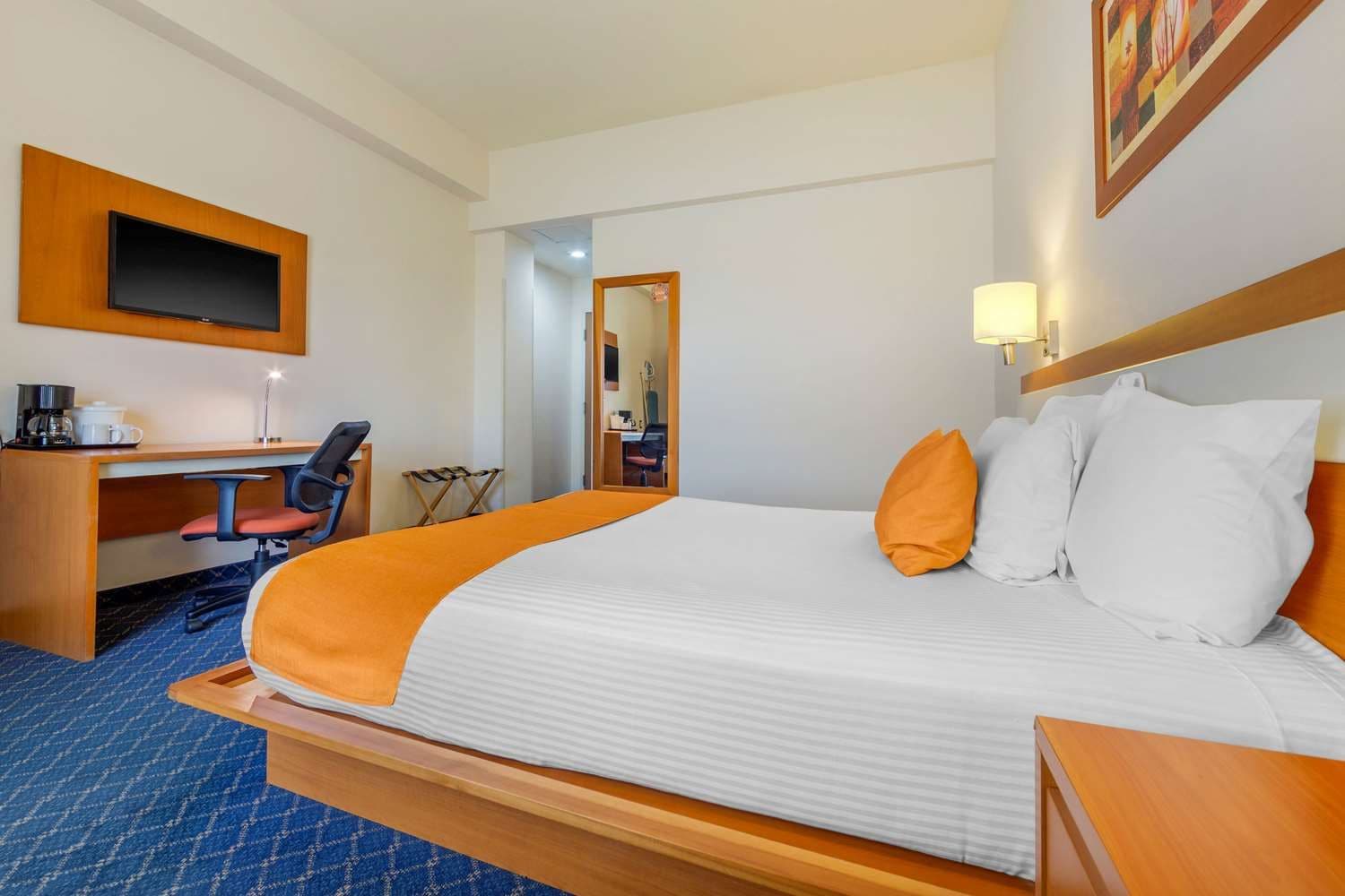 Ein Hotelzimmer mit Bett, Schreibtisch, Stuhl, Fernseher und Spiegel.