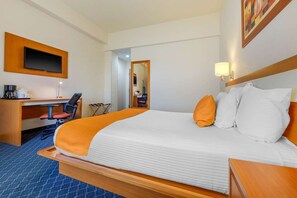 A hotel room with a bed, a desk, a chair, a television, and a mirror.