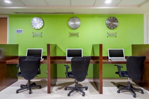 A room with three desks, each with a laptop and a black office chair. There are three wall clocks above the desks.