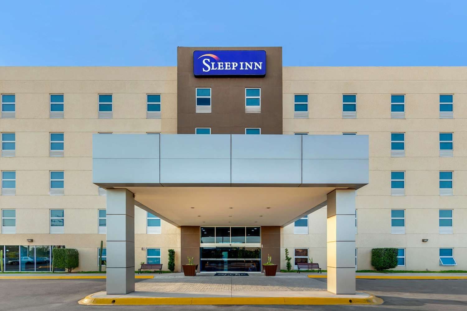 Un hotel Sleep Inn con entrada central, varias ventanas y un cielo azul despejado.