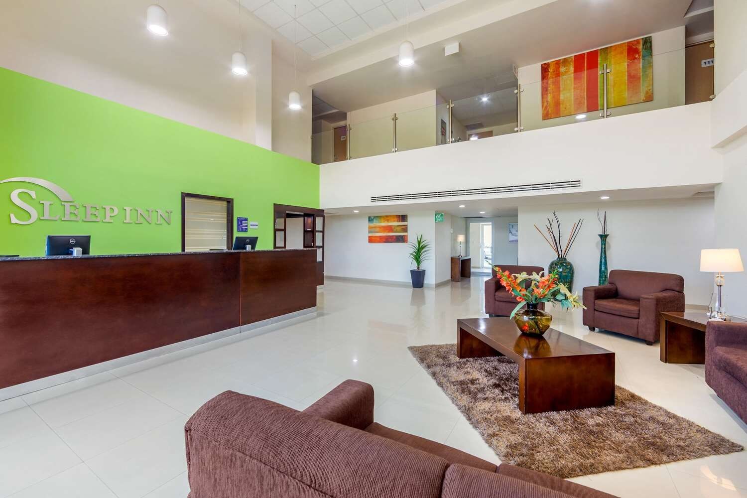 Vestíbulo de hotel con mostrador de recepción, zona de estar y escalera que lleva a un nivel superior.
