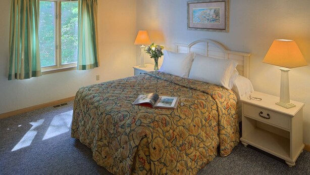 A bedroom with a bed, two bedside lamps, a nightstand, a framed picture on the wall, and a window with curtains.