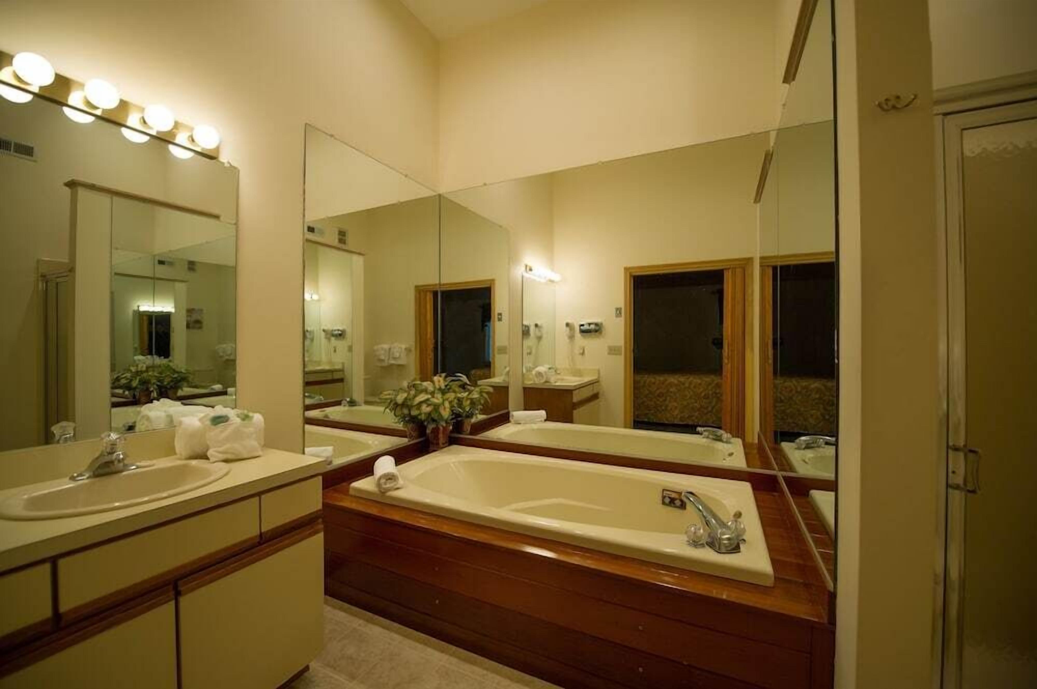A bathroom with a large mirror, two sinks, a bathtub, and wooden flooring.