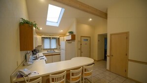 A compact kitchen with a central island, a dining area with chairs, a small refrigerator, and a window with a view.