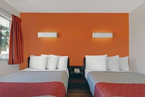 Ein Hotelzimmer mit zwei Betten, orangefarbenen Wänden und einem Fenster mit Vorhängen.