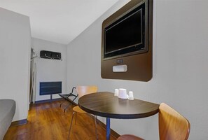 Ein Zimmer mit einem runden Tisch, zwei Stühlen, einem Flachbildfernseher an der Wand, einem Kleiderständer und einem kleinen Regal.