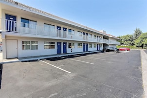 Un motel con estacionamiento, varias habitaciones con puertas azules y una estructura de dos pisos.