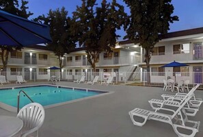 A swimming pool with lounge chairs and tables, surrounded by a fenced area with a multi-story building in the background. - Park Inn by Radisson, San Jose (San Jose)