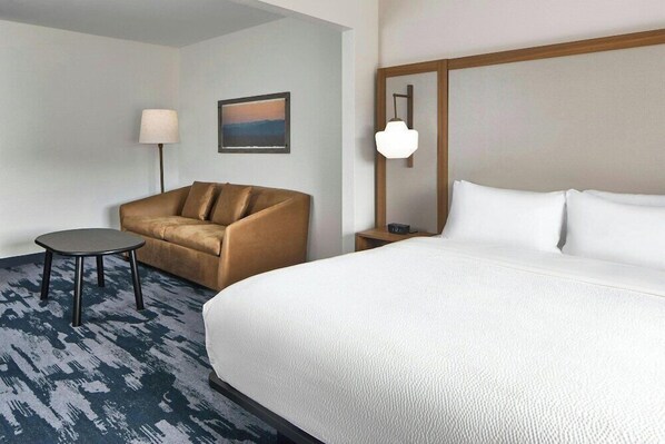 Habitación de hotel con una cama grande, un sofá, una mesita, una lámpara y un cuadro en la pared.