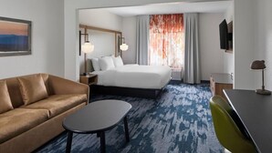 Quarto de hotel com cama, sofá, escrivaninha, cadeira, televisão e um quadro na parede.
