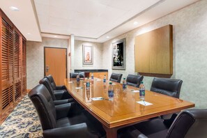 Un salón de conferencias con una larga mesa, sillas de cuero negro y botellas de agua.