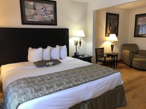 Una habitación de hotel con una cama grande, un escritorio, dos sillas y un cuadro en la pared.