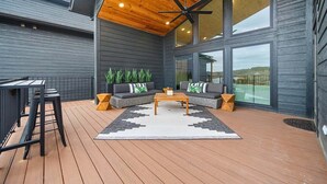 Un espacio exterior techado con mobiliario que incluye una barra, un sillón, un sofá y una mesa de centro.
