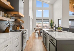 A modern kitchen with white cabinetry, a central island, and a dining area with a view. - Private Pool, Dock, Movie Room on Lake Hamilton (Hot Springs)