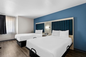 Habitación de hotel con dos camas, una mesita de noche con lámpara y una ventana con cortinas.