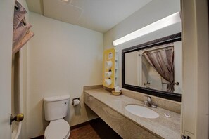 A bathroom with a toilet, sink, mirror, towel dispenser, and a shower curtain. - Park Inn by Radisson, Medical Center (San Antonio)