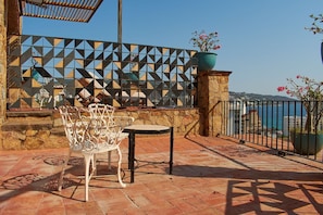 Eine Terrasse mit Tisch und Stühlen, eine geometrische Wand und Blick aufs Meer.