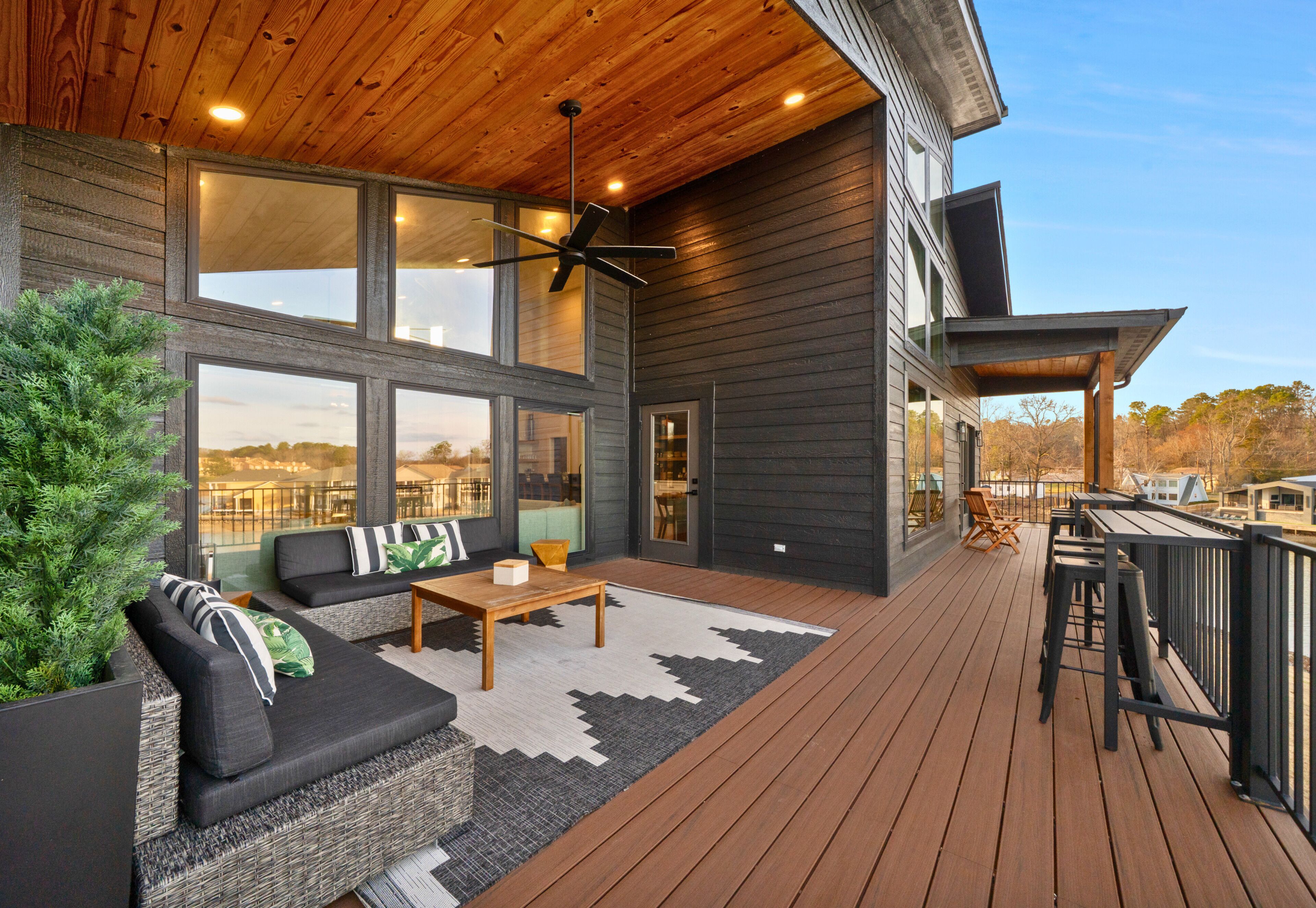 A modern outdoor deck with a wooden floor, a black sofa with striped cushions, and a small table.