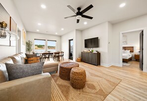 A spacious living area with a ceiling fan, a dining table with chairs, a television mounted on the wall, and a bedroom visible through an open door. - The Great Escape - 1 (Hot Springs)