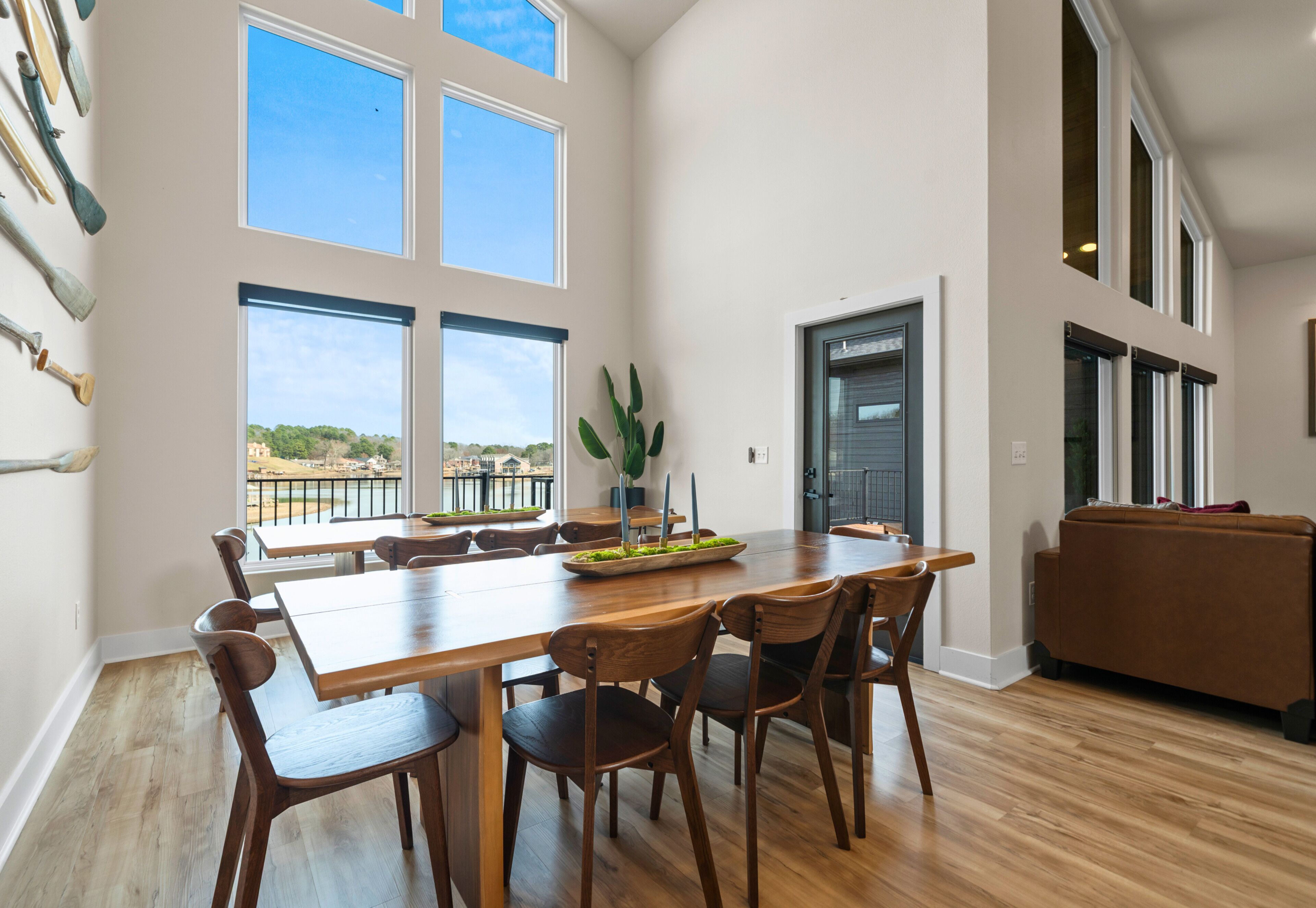 Un vaste espace de salle à manger avec une grande table et des chaises en bois, de grandes fenêtres offrant une vue dégagée et une entrée moderne donnant sur la cuisine.