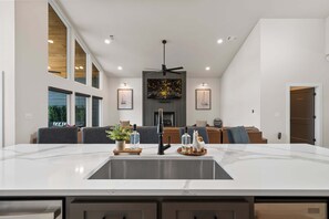 Eine moderne Küche mit einer großen Kochinsel, Einbau-Deckenleuchten und einem Essbereich mit einer Couch und Stühlen.
