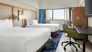 Ett hotellrum med två sängar, ett skrivbord, en stol och ett stort fönster.