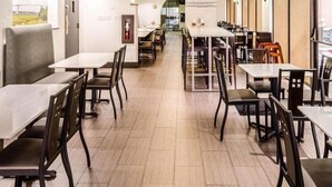En restaurang med flera bord och stolar, en platt-TV som är monterad på väggen och en brandsläckare på väggen.