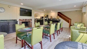 Un comedor con mesas y sillas redondas, una chimenea, una zona de cocina y una escalera.