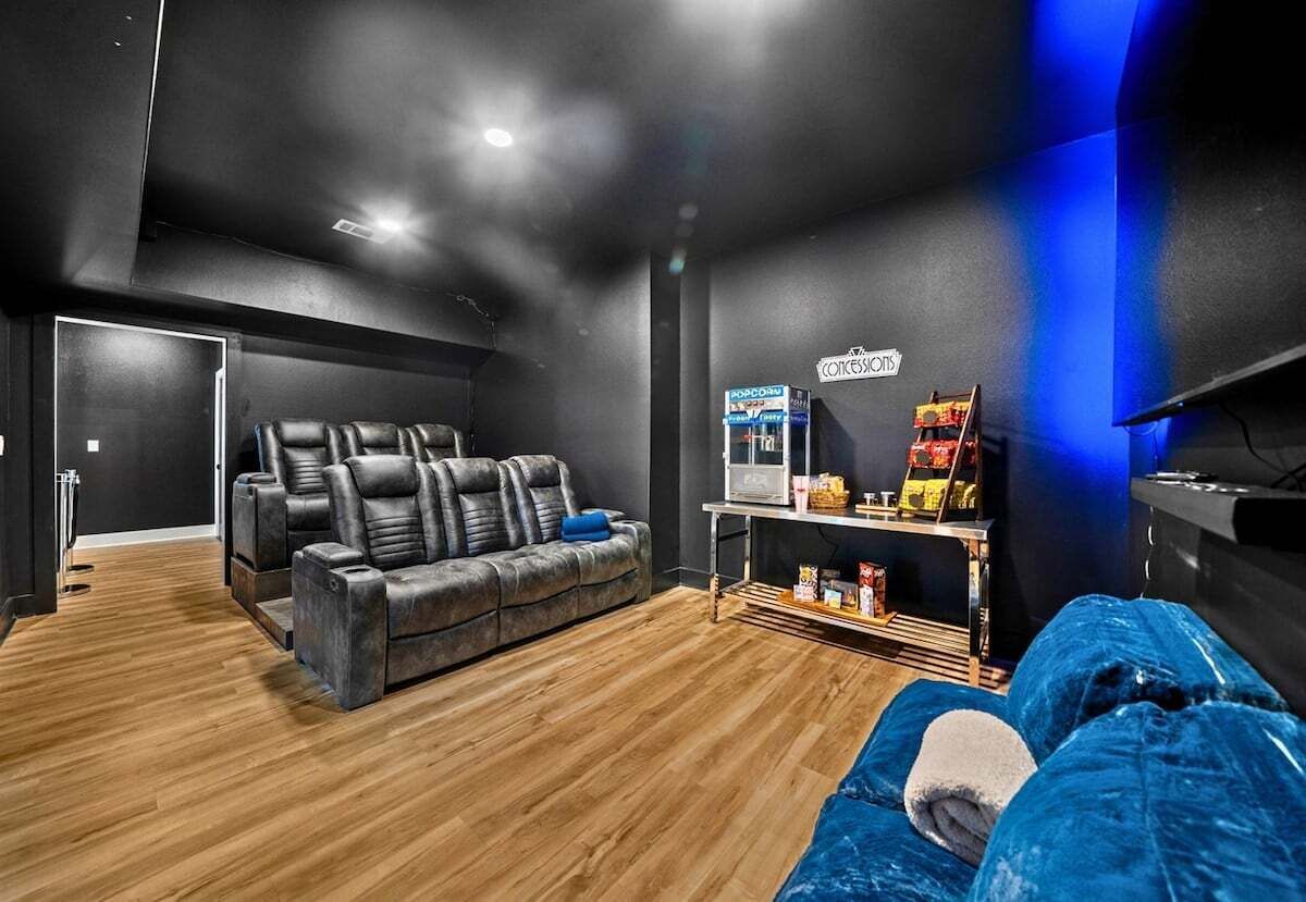 Una habitación moderna con una paleta de colores oscuros, un sofá de cuero, un sillón reclinable, un televisor y una zona de bar con aperitivos.