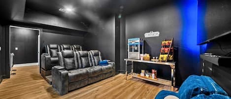 Una habitación moderna con una paleta de colores oscuros, un sofá de cuero, un sillón reclinable, un televisor y una zona de bar con aperitivos.