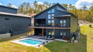 A two-story modern house with a swimming pool, a covered patio, and a view of the surrounding forest. - Private Pool, Dock, Movie Room on Lake Hamilton (Hot Springs)