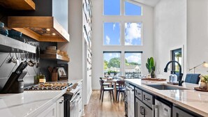 A modern kitchen with white cabinetry, a central island, and a large window overlooking a green landscape. - Private Pool, Dock, Movie Room on Lake Hamilton (Hot Springs)