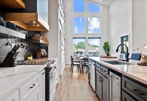 A modern kitchen with white cabinetry, a central island, and a large window overlooking a green landscape. - Private Pool, Dock, Movie Room on Lake Hamilton (Hot Springs)