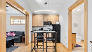 A compact kitchen with wooden cabinets, a black refrigerator, a microwave, and a coffee machine.