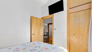 A bedroom with a bed, a wooden wardrobe, and a door leading to a dining area.
