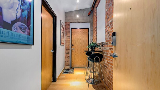 A hallway with wooden doors, a brick wall, a small table with chairs, and a poster on the wall.