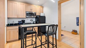 A compact kitchen with wooden cabinets, a microwave, a toaster, and a small dining table with two chairs.