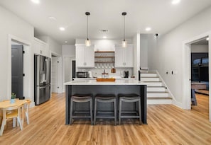 A modern kitchen with a central island, bar stools, stainless steel appliances, and pendant lighting. - Private Pool, Dock, Movie Room on Lake Hamilton (Hot Springs)