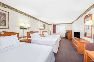 Una habitación de hotel con tres camas, televisión, escritorio y espejo.