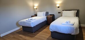A hotel room with two beds, each with a pillow and a towel, a nightstand, and a wall-mounted light. - Staindrop Lodge Hotel (Sheffield)