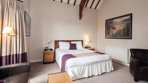 A hotel room with a bed, bedside tables, a chair, a desk, a radiator, and a painting on the wall. - Staindrop Lodge Hotel (Sheffield)