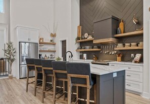 Eine moderne Küche mit einer zentralen Kochinsel, Barhocker und Holzregalen mit Küchenutensilien.