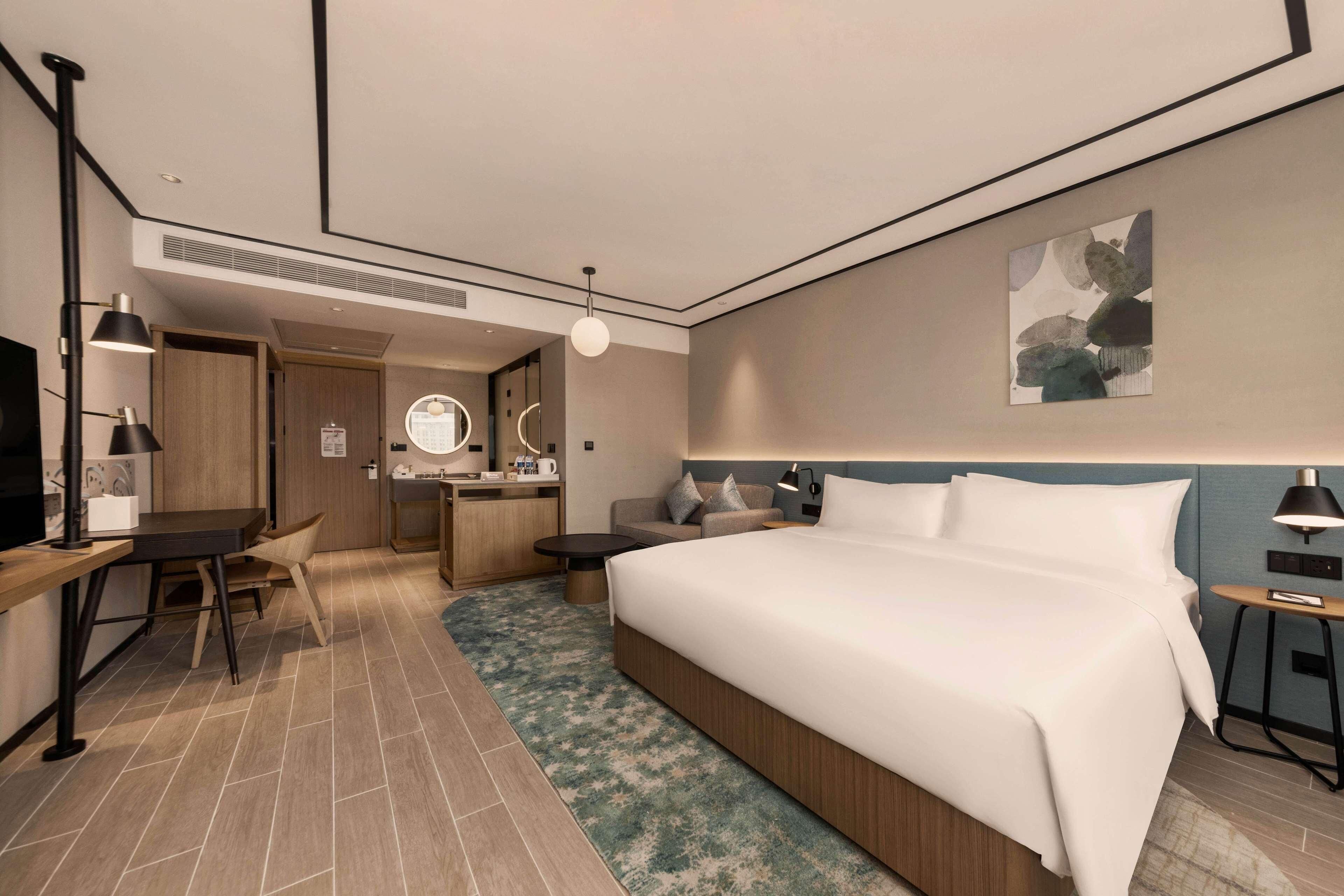 Une chambre d’hôtel moderne équipée d’un grand lit, d’un bureau, d’une chaise, d’une petite table, d’une télévision et d’une salle de bain.
