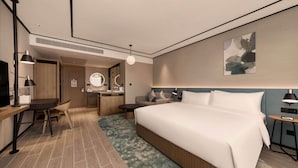 Ein modernes Hotelzimmer mit einem großen Bett, einem Schreibtisch, einem Sessel, einem kleinen Tisch, einem Fernseher und einem Badezimmer.