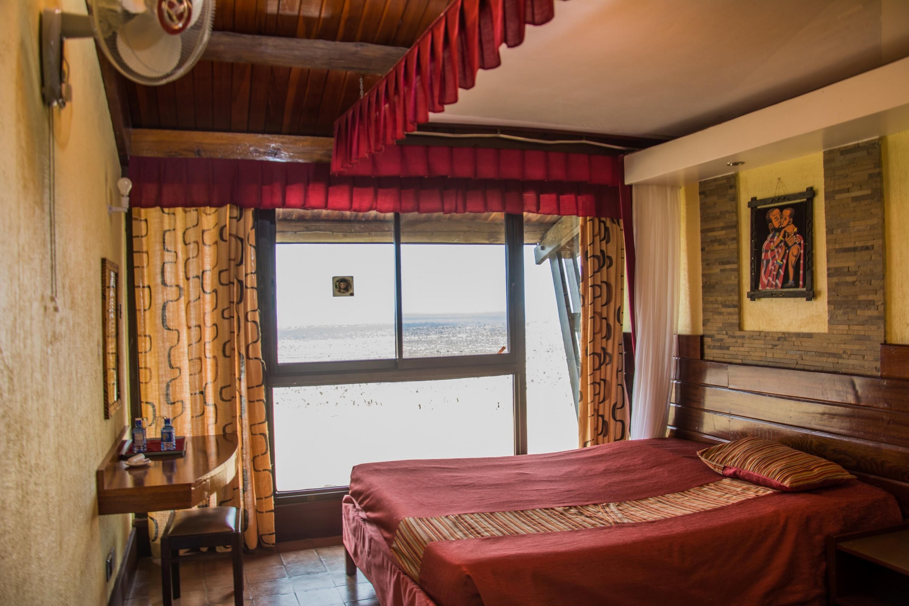 A room with a bed, a desk, a chair, a window with curtains, and a wall with a framed picture.