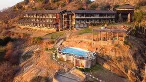 Un hotel de varios pisos con piscina, arquitectura de piedra y vistas a las colinas circundantes.