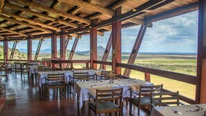 Un comedor interior con mesas y sillas, ventanas amplias y vistas al paisaje.
