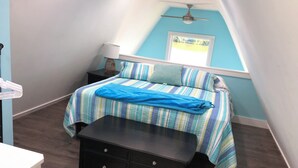 Une chambre avec un plafond en pente, un lit avec une literie à rayures, une table de chevet avec une lampe et une fenêtre donnant sur un beau paysage.