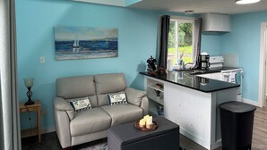 Une cuisine moderne avec un îlot central, un coin repas avec un canapé et des coussins, et un tableau représentant un voilier accroché au mur.